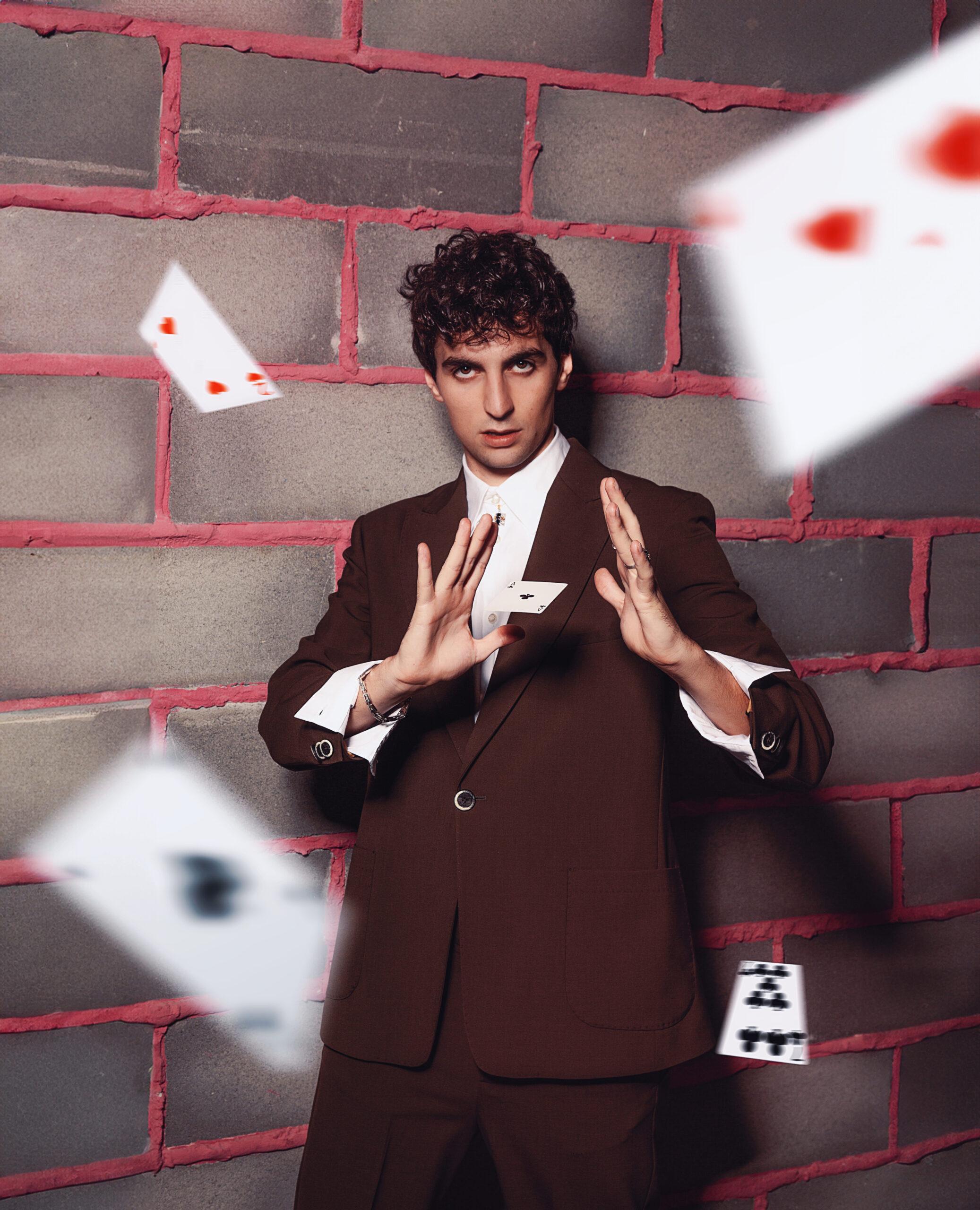 uomo che guarda l'obbiettivo con carta sospessa in mano, carte che volano intorno a lui