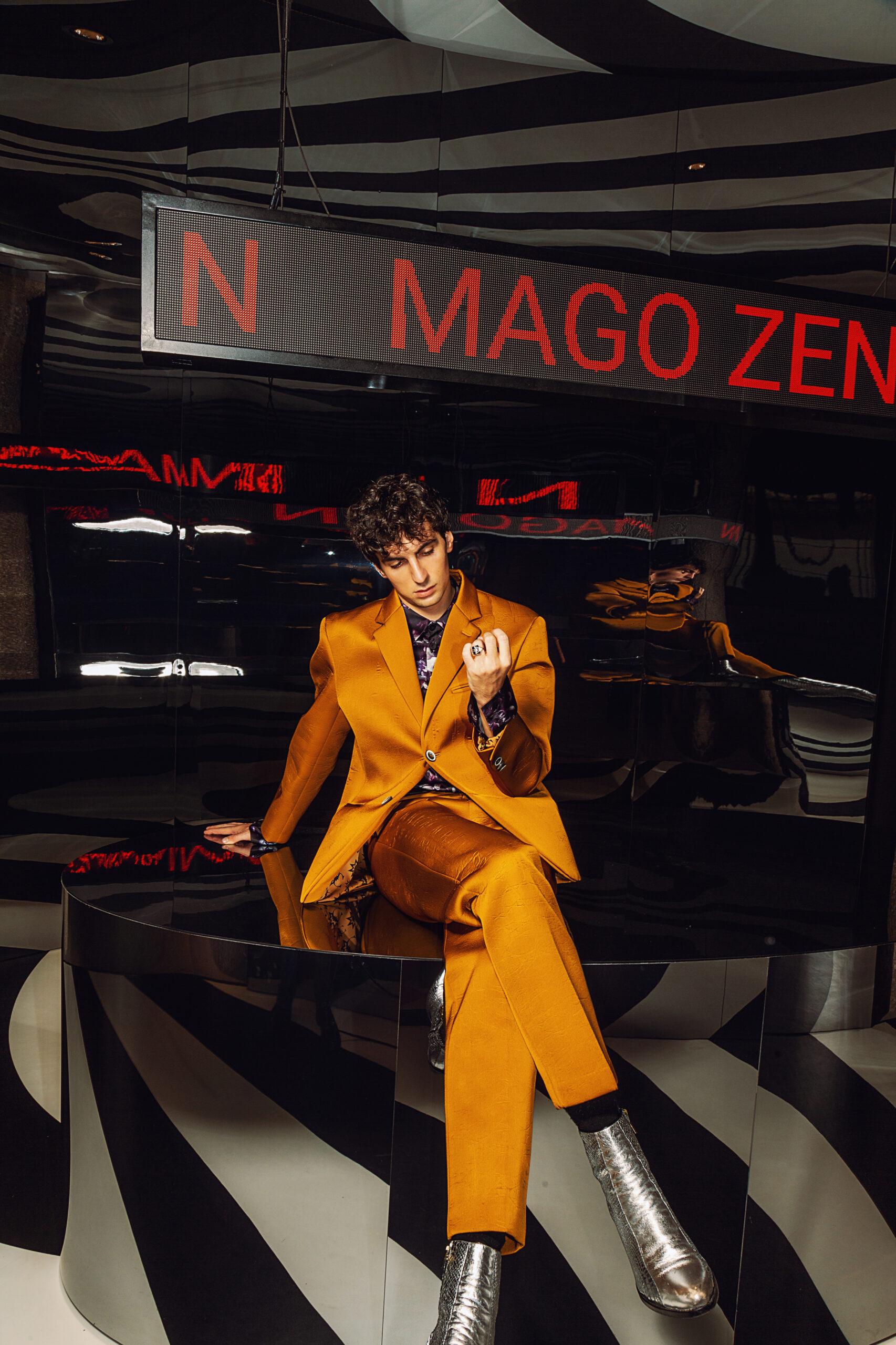 Uomo seduto con gambe incrociatte indossando un abito colore senape